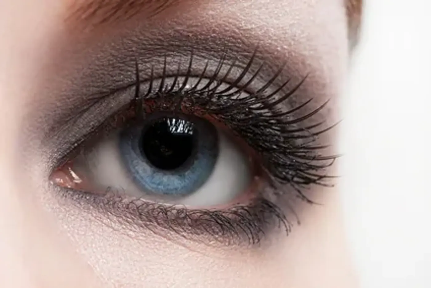 Main appliquant du mascara noir sur les cils supérieurs d’un œil maquillé