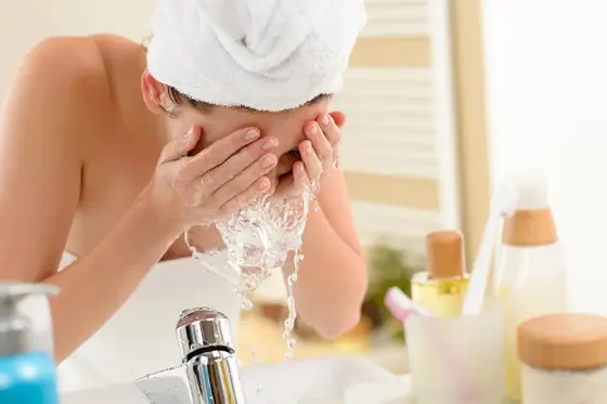 Flacon ambré d’eau florale vaporisé au-dessus d’un visage propre