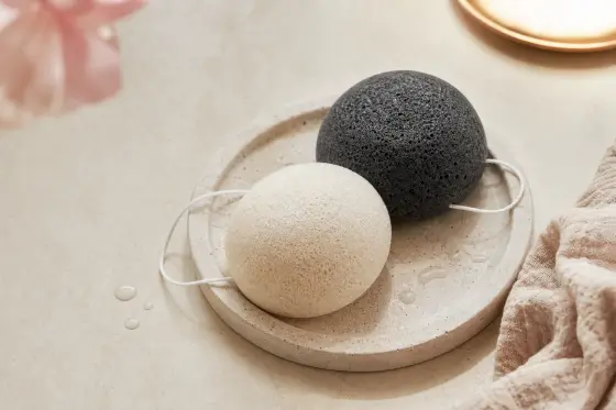 Main tenant une éponge konjac ronde et humide au-dessus d’un lavabo de salle de bains