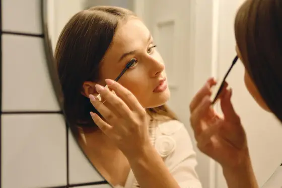 Main tenant une brosse de mascara près d’un œil maquillé aux cils séparés