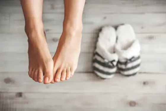 Pieds enveloppés dans des chaussettes en maille, près d’une crème et d’une serviette